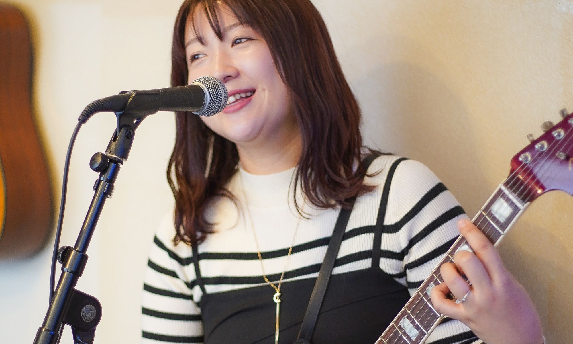 : 女性シンガーがギターを抱えて歌いながら演奏する写真。TANNY音楽教室のギター＆ボーカルコースイメージ
