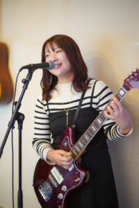 福岡市西区のギター教室、TANNY音楽教室でエレキギターを弾きながら笑顔で歌う大人の女性生徒さん