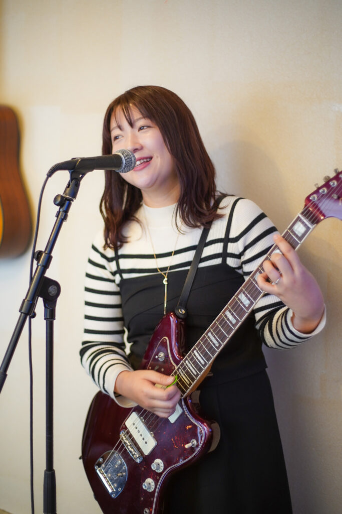 福岡市西区のギター教室、TANNY音楽教室でエレキギターを弾きながら笑顔で歌う大人の女性生徒さん